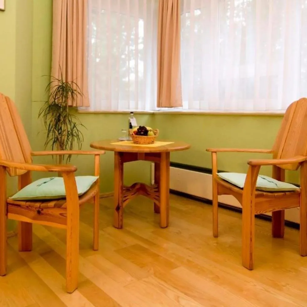 Sitzecke mit zwei Holzsesseln und rundem Tisch am Fenster