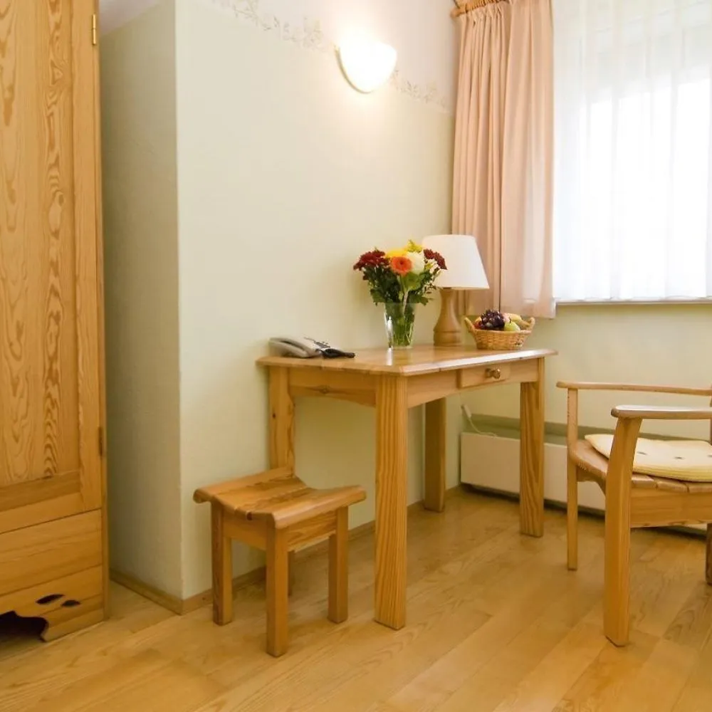 Holzschreibtisch mit Blumenstrauß, Hocker und Kleiderschrank im Einzelzimmer